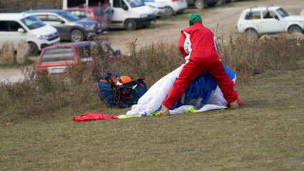A paraglider assembles his paraglider after landing. In the background is a parking lot.
