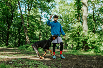 Man training doberman pinscher with leash in forest