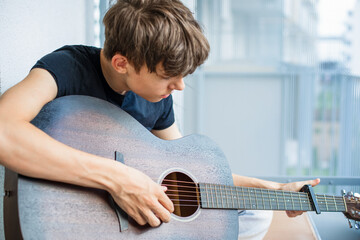 A teenager enthusiastically learns to play the guitar and tunes the strings in his free time while...