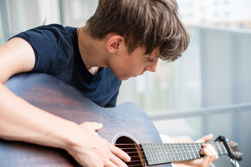 A teenager enthusiastically learns to play the guitar and tunes the strings in his free time while...