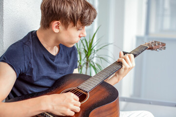 A teenager enthusiastically learns to play the guitar and tunes the strings in his free time while...