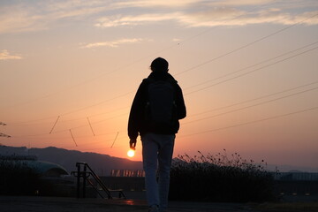 Person with backpack walking into the sunset – backlit city scene