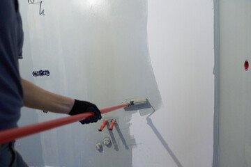 A man paints the inner wall of his house. Apartment renovation. Concrete walls are painted with a paint roller. High quality photo