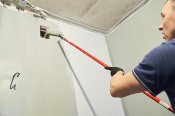 A man paints concrete walls with a paint roller. Gray paint creates a cozy atmosphere in the room. High quality photo