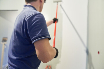 Men's hands paint walls with a roller, work painting on the surface, painting walls in an apartment, repair with white paint. With space to copy. High quality photo