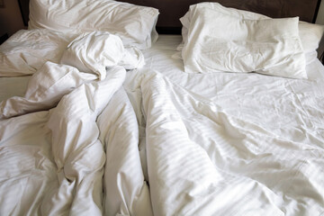 The unmade bed with bed with cotton bedclothes in hotel. Close-up of unfinished or messy bed. Rumpled white bedding sheets and pillow. Room service. Sunday loneliness relaxing
