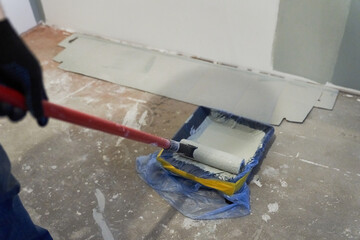 A container of paint for a paint roller. Apartment renovation. Concrete walls are painted gray with a paint roller. High quality photo
