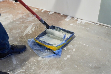 A container of paint for a paint roller. Apartment renovation. Concrete walls are painted gray with a paint roller. High quality photo