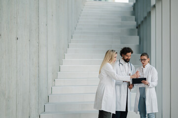 Medical team discussing patient data on digital tablet in hospital stairwell
