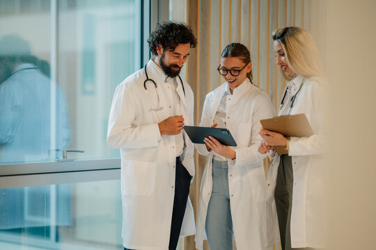 Medical team discussing patient data using digital tablet in hospital corridor