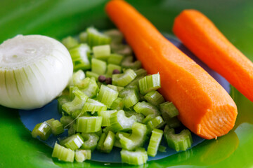 
Fresh vegetables are visible on the green surface – half an onion, chopped celery stalks and two whole carrots.