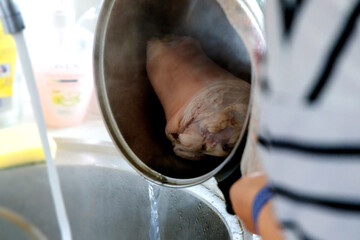 
a person holding a pot or pan under a stream of water from a faucet, and a piece of meat is visible inside the pot.