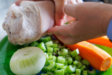 
hands holding a large piece of meat above a plate of sliced ​​vegetables including celery stalks, onion and carrots.