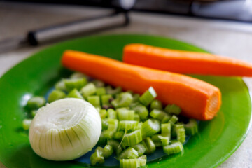 
The green plate displays fresh vegetables, including half a peeled onion, chopped celery stalks,...