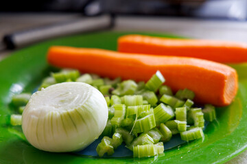 The green plate displays fresh vegetables, including half a peeled onion, chopped celery stalks, and two whole carrots.