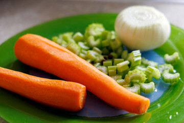 
Fresh vegetables are displayed on a green plate, including two peeled carrots, chopped celery stalks, and half an onion.