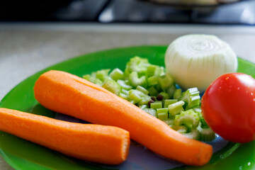 
Fresh vegetables are displayed on a green plate, including two peeled carrots, sliced ​​celery stalks, half an onion, and one tomato.