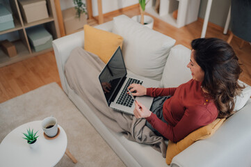 Woman shopping online using laptop and credit card on sofa at home