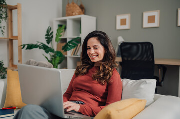 Woman working from home using laptop on sofa smiling