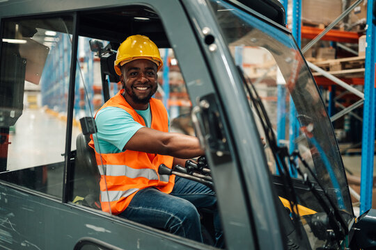 Smiling warehouse worker driving forklift in logistics center