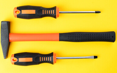 Two screwdrivers and hammer on yellow background, top view hand tools set