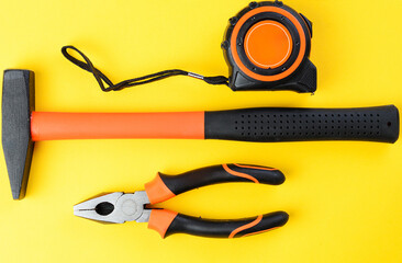 Pliers, hammer and tape measure on yellow background, top view tools set