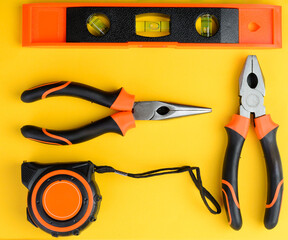 Two pliers, tape measure and level tool top view on yellow background