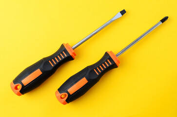 Flat and Phillips screwdrivers on yellow background, minimal layout with repair tools