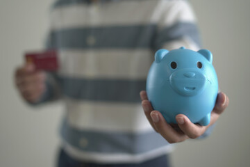 Young asian man holding credit card and piggy bank for shopping and paying online, ordering...