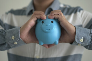 Young asian man is holding the piggy bank and putting cash coins for financial saving for the...
