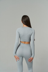 A woman with long dark hair is facing away, wearing a light gray fitted top and high-waisted...