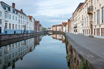 A serene scene featuring a historic Bruges cityscape with traditional buildings reflected in the calm canal water, complementing the tranquil and picturesque environment.