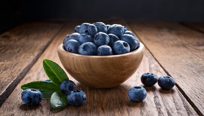 ripe blueberries in wooden bowl on rustic wood surface with green leaf