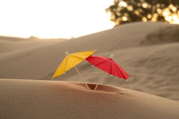 Miniature Yellow and Red Cocktail Paper Umbrellas on Sand Dunes at Sunset