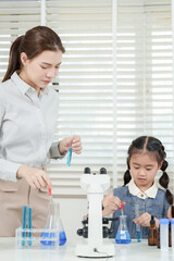 Caucasian female teacher watching asian girl using pipette during classroom science experiment with...