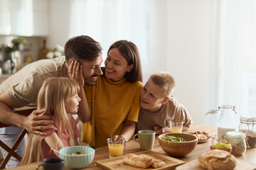 Young parents and their small kids talking while having breakfast in dining room.