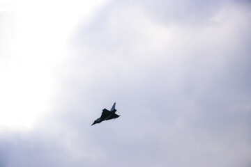Military fighter jet in flight against a clear pale blue sky. Dark silhouette of aircraft with...