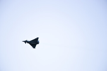 Military fighter jet in flight against a clear pale blue sky. Dark silhouette of aircraft with...