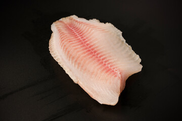 Fresh tilapia fillet on black background, top view.