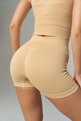 Athletic woman in beige ribbed sportswear highlighting form, posed from the back, showcasing fitted shorts and top, focusing on toned body and smooth fabric texture