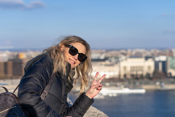 Tourist blonde woman posing with peace sign over Danube river in the background of winter Budapest...