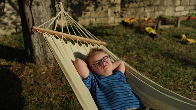 Cute little boy with Down syndrome relaxing in hammock. Summer, vacation, family gathering. 