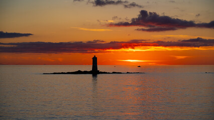 Peaceful lighthouse silhouette during vivid orange sunset over calm ocean waters