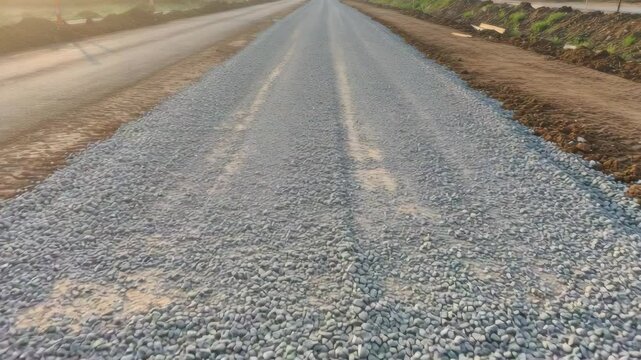 Gravel road base prepared for asphalt paving, showing realistic surface texture and early morning light &mdash; symbolizing road construction groundwork.
