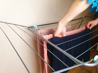 A housewife hangs washed laundry on the dryer. Laundry dryer, drying rack for washed wet clothes.