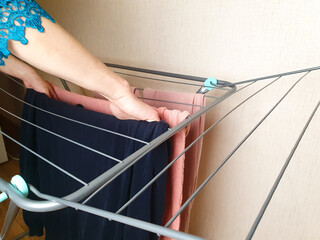 A housewife hangs washed laundry on the dryer. Laundry dryer, drying rack for washed wet clothes.