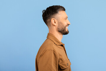 Side view of smiling young man standing confidently. Modern male model with short hair and beard in...
