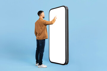 Back view of young man interacting with large blank smartphone screen. Ideal for futuristic app...