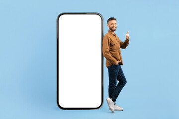 Cheerful young man standing with thumbs up next to big smartphone mockup. Ideal for app marketing, mobile UI design, or tech startup concepts on blue background, collage