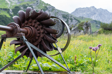 Old iron water wheel standing on lush meadow in alpine landscape as monument 1